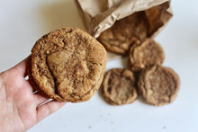 Load image into Gallery viewer, Four Churrodoodle cookies spilling out of brown paper bag and the model hold a Churrodoodle closer to the camera.
